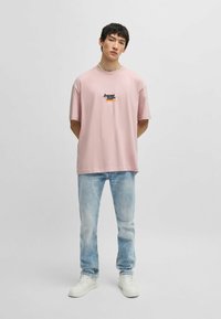 Camiseta de algodón rosa con cuello redondo, mangas cortas y gráfico en el pecho. Combinada con unos vaqueros de mezclilla azul claro y zapatillas blancas.