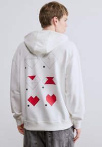 Λευκό φούτερ με κουκούλα που διαθέτει γραφικά σε στυλ οριγκάμι με κόκκινες και μαύρες καρδιές στην πλάτη, με κουκούλα με κορδόνι και ριμπ μανσέτες και τελείωμα.