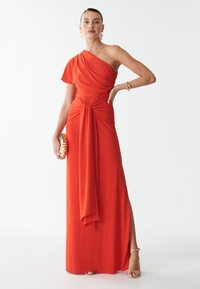 Sarkans, vienpusējs vakartērps ar drapētiem audumiem un pagrieziena detaļu jostasvietā, ar sānu šķēlumu un zelta clutch somiņu. Mākslīgi mīksta tekstūra.
