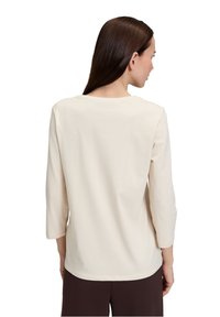 Langärmliges Shirt aus einem hellen Creme-Stoff, mit Rundhalsausschnitt und lockerer Passform. Glatte Textur mit einfachem Design, keine sichtbaren Muster.