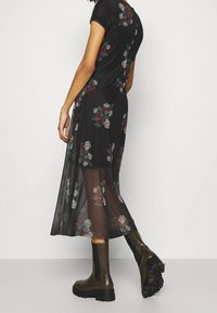 Svart blommig klänning med korta ärmar, genomskinligt tyg och flerfärgade blommönster; matchad med mörka, kraftiga stövletter.