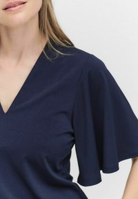 Mörkblå V-ringad topp med korta, utsvängda ärmar, tillverkad av ett slätt, mjukt tyg. Har en ren design utan synliga mönster eller accenter.