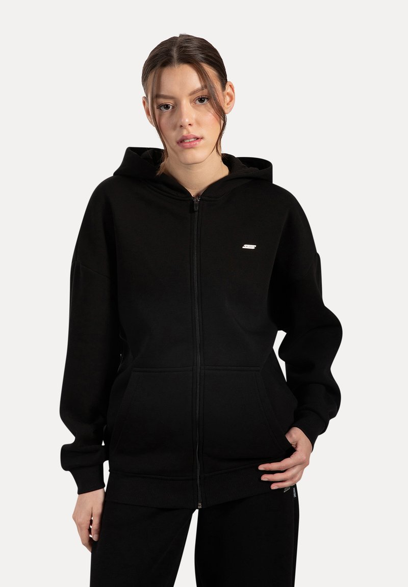 Czarna bluza z kapturem na zamek, wykonana z miękkiego materiału, z przednią kieszenią, ściągaczami na rękawach i małym logo na lewej piersi. Prosty design.