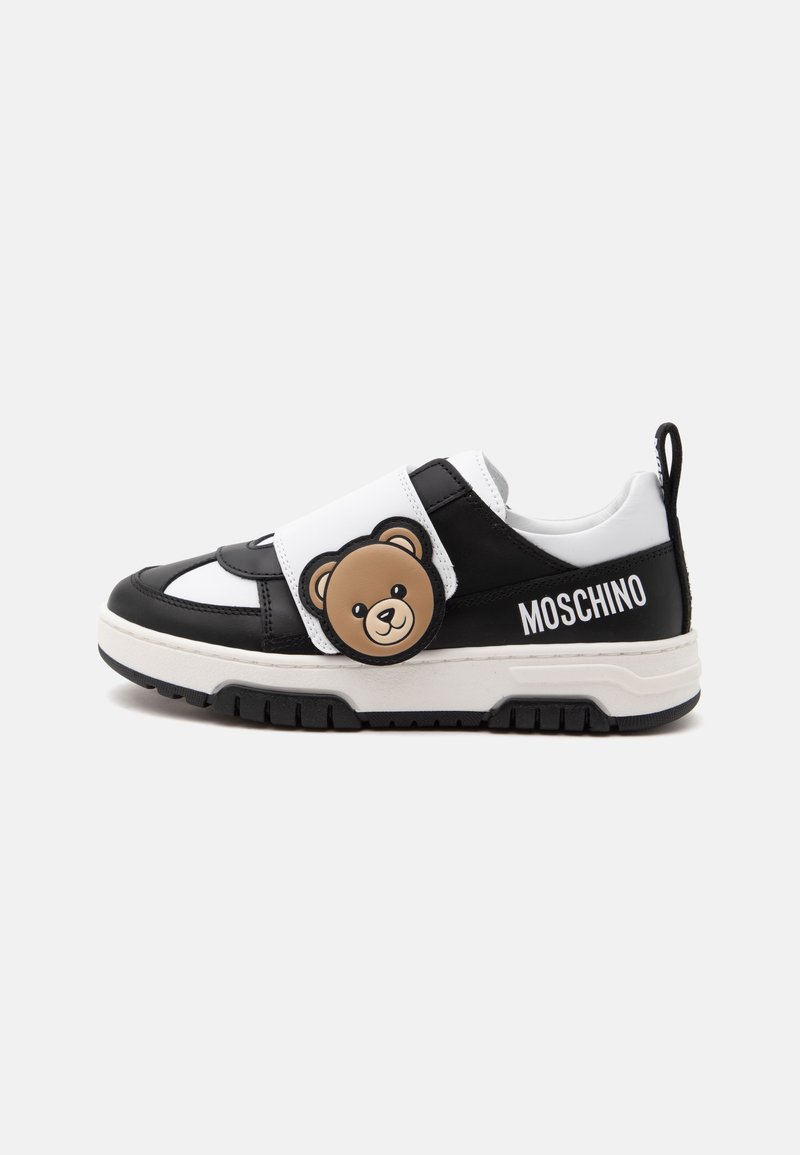 Ασπρόμαυρο sneaker Moschino με καφέ πρόσωπο αρκουδάκι στο λουράκι και το όνομα της μάρκας στο πλάι.