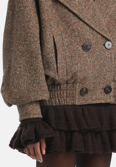 Brown herringbone patterned oversized coat with large black buttons. Features puffed sleeves and an elastic waistband. Black ruffled knit skirt.