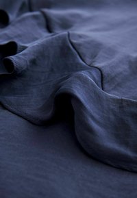 Granatowy materiał o gładkiej fakturze, z delikatnymi fałdami i łagodnymi krzywiznami. Materiał wydaje się lekki i przepuszczający powietrze, z matowym wykończeniem.