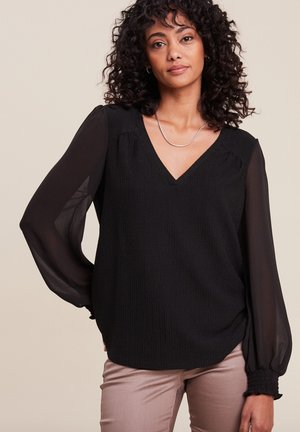 Blouse noire avec un corps texturé, des manches longues transparentes, un décolleté en V et des détails froncés aux épaules et aux poignets.