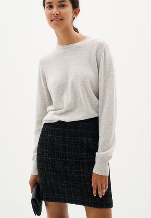 Lichtgrijze, lange mouw trui van zachte brei, gecombineerd met een aangesloten zwarte textuurskirt. Accessoires zijn onder andere een kleine zwarte clutch.
