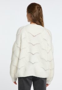 Maglione bianco oversized in maglia con un motivo a onda testurizzato, vestibilità ampia e spalle scese. Tessuto morbido con dettagli di cucitura visibili.