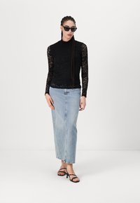 Must mustriga pikkade varrukatega must pitsist särk kõrge kaelusega, kombineeritud helesinise denimpikkseeliku ja mustade rihmadega sandaalidega, luues kihilise välimuse.