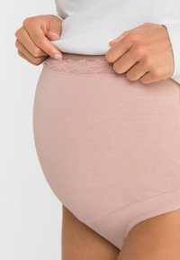 Slip taille haute rose clair avec une texture lisse et une bordure en dentelle à la taille. Présente un design sans coutures pour un confort optimal.