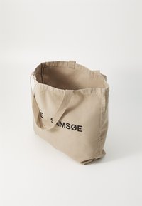 Beige Canvas-Shopper mit schwarzem Text "SAMSØE" auf der Vorderseite, aus robustem Stoff und mit doppelten Schulterriemen für ein einfaches Tragen.