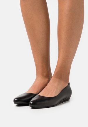 Bottines en cuir noir à talon compensé avec une semelle arrondie et une texture lisse, dotées d'un talon bas et d'un design minimaliste.