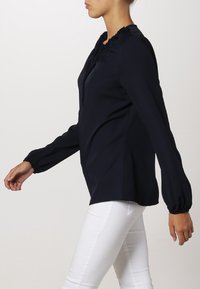 Námořnická blůza s dlouhým rukávem, texturovaným výstřihem a nabíranými rukávy, vyrobená z hladkého materiálu, spárovaná s bílými přiléhavými kalhotami.