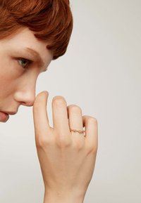 Anillo de oro rosa con pequeñas piedras de color rosa claro engastadas en una delicada banda retorcida. Presentado a mano con los dedos parcialmente curvados.