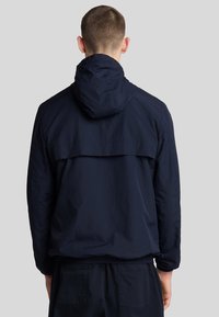 Marineblå, letvægtsjakke med hætte, der har struktureret stof, elastiske manchetter og en bagventil design. Sømløs konstruktion fremhæver pasformen.