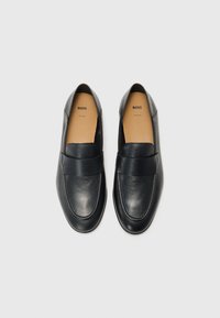 Black leather slip-on shoes with a smooth texture, almond-shaped toe, and a wide strap across the instep. Designed for comfort and ease.