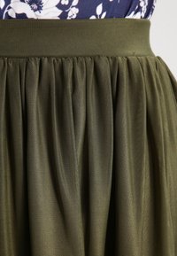 Jupe en mesh vert olive avec taille froncée, associée à un haut à motif floral navy au niveau de la taille.