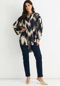 Navy and beige patterned blouse with a button front, relaxed fit, and long sleeves, paired with dark jeans and gold heels.