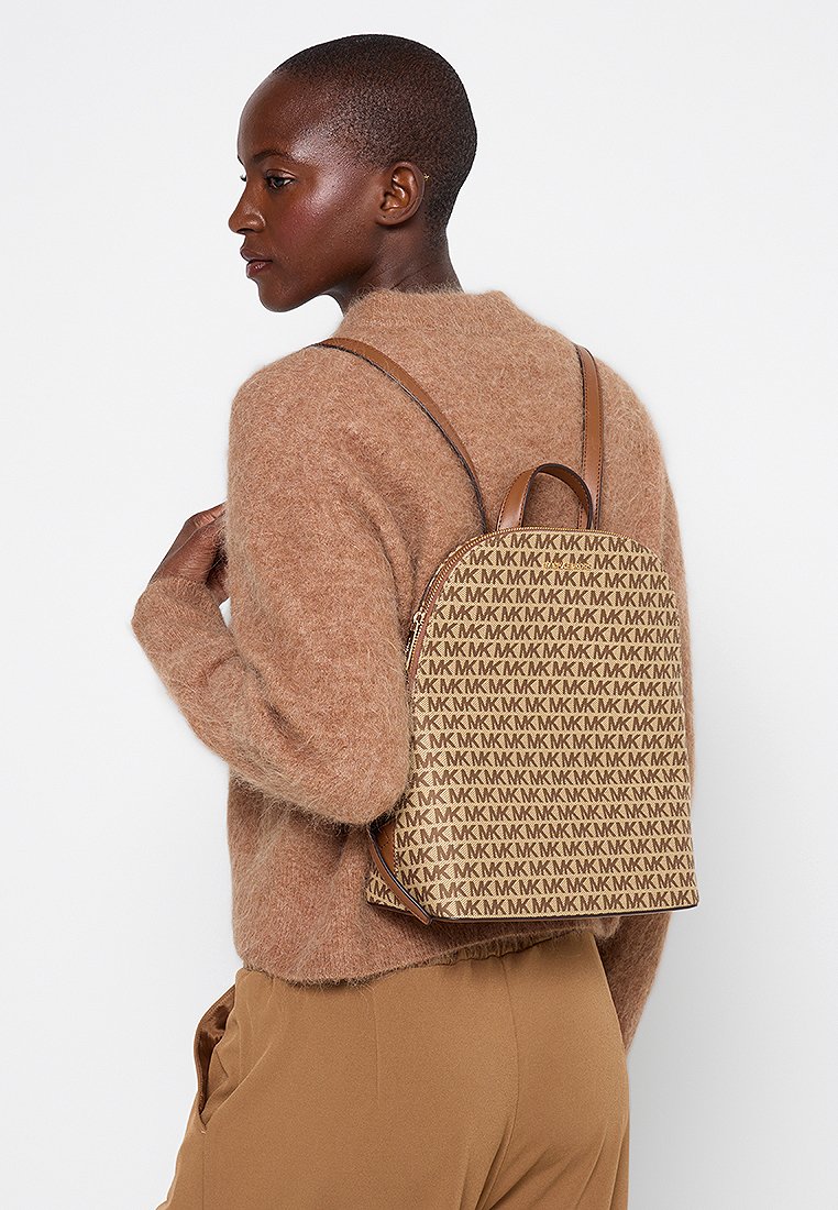 Zaino beige a fantasia realizzato in tessuto con una superficie liscia, dotato di spallacci in pelle marrone e forma arrotondata, indossato sulla schiena.