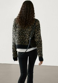 Mustikkatäpläinen neulepaita mustana ja ruskeana, löysällä istuvuudella ja ribbauslahkeilla, käytetty valkoisen paidan päällä ja yhdistetty mustiin housuihin.