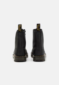 Stivali ankle in pelle nera con cuciture gialle, punta tonda e pannelli laterali elastici. Presentano linguette per l'estrazione e suole in gomma texturizzate.