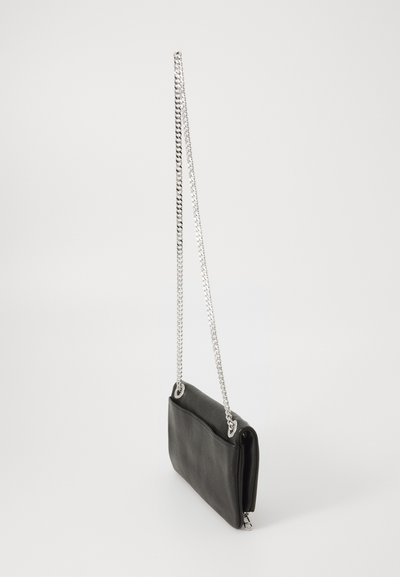 Small black leather crossbody bag with silver chain strap hanging against a white background.