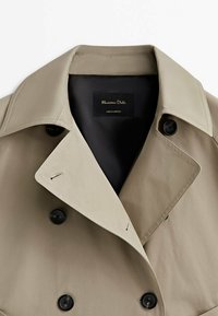 Beige kaksirivinen trenssitakki mustilla napeilla ja leveillä kauluskäänteillä, merkitty Massimo Dutti, mustalla vuorella.