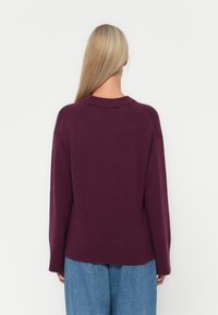 Maglione lavorato a maglia viola con colletto e orlo a coste, caratterizzato da una vestibilità rilassata e maniche lunghe. Vista posteriore mostrata, abbinato a jeans azzurri chiari.