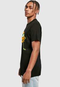 Black cotton t-shirt featuring a colorful cartoon character on the front. Short sleeves, crew neck, relaxed fit, with a smooth texture.