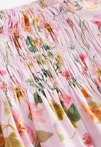 Gros plan d’un tissu rose avec des fronces élastiques et un motif floral multicolore avec des feuilles vertes et diverses fleurs.