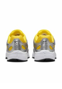 Sportliche Schuhe mit einem gelben Mesh-Obermaterial und silbernen synthetischen Akzenten, ausgestattet mit gepolsterten Kragen, sichtbaren Luftpolstern und strukturierten weißen Sohlen.