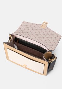 Svart och beige handväska med en strukturerad design, som har en guldkedjesträng och en ficka med dragkedja inuti. Inuti finns ett rosa mönstrat foder.