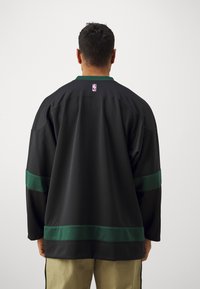 Čierny dres s zelenými akcentmi, zaobleným výstrihom a športovým strihom. Logo NBA na zadnej strane, so štruktúrovanou tkaninou.