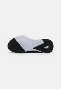 Semelle de chaussure de sport en noir et blanc avec des motifs texturés, comportant un logo bien visible, et en caoutchouc flexible pour une traction et un soutien.