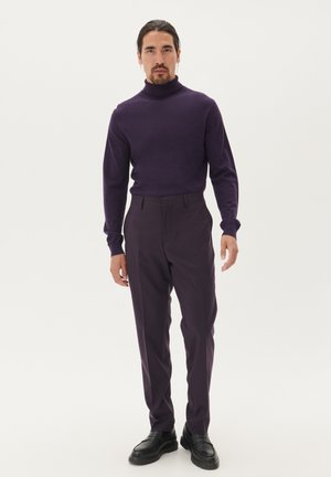 Lila Rollkragensweater kombiniert mit passenden lila Hosen. Das Outfit zeichnet sich durch eine glatte Textur und eine taillierte Silhouette aus, abgerundet mit schwarzen Schuhen.
