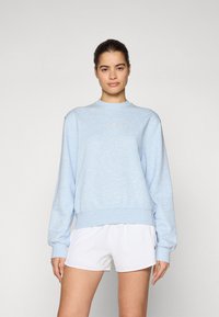 Light blue sweatshirt made of soft fabric with a round neckline, ribbed cuffs, and a small logo detail on the chest; paired with white shorts.