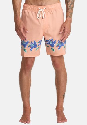 Men’s peach swim shorts with blue floral pattern along the bottom, white drawstring waistband, worn by a standing, barefoot male model.