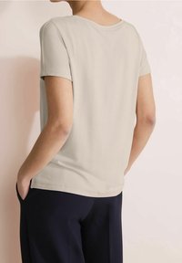 Ljusbeige kortärmad topp med rundad halsringning, avslappnad passform och en slät yta, tillsammans med mörkblå byxor.