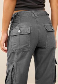 Pantalon cargo gris avec poches latérales, coupe décontractée et texture de tissu douce. Des boutons ornent les poches pour un détail supplémentaire.