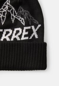 Zwarte gebreide beanie met witte en grijze graphics, waaronder de tekst "TERREX" en bergontwerpen. Geribbelde manche aan de onderkant.