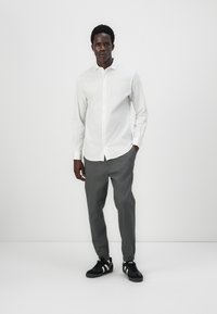 Hvit langermet skjorte med krage og knappestolpe, kombinert med grå tapered bukser og svarte sneakers med hvite striper.