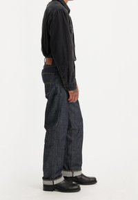 Mörk denimjeans med uppvikt fåll, orange sömmar och en läderetikett bak. I kombination med en svart långärmad tröja och svarta stövlar.