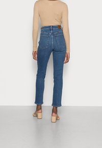 Höga blå denimjeans med en åtsittande silhuett, bakfickor och en slät textur. Parat med en beige ribbad långärmad topp.