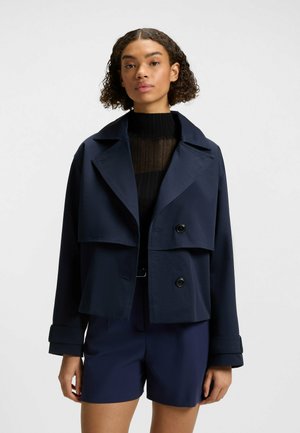 Navy blue cropped jacket in a smooth material with a wide lapel, two buttons, and rolled cuffs, paired with a black knit top and navy shorts.