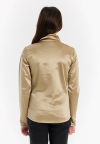 Langarmige, metallic gouden top met een hoge kraag, een soepele textuur en een getailleerd ontwerp. De achterkant heeft een lichte bocht bij de zoom.