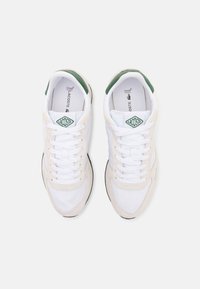Lacoste-sneakers i hvit mesh og kremfarget semsket skinn med grønn aksent. Har en polstret såle og klassisk snøring.