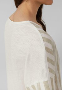 Lichtgekleurde shirt met korte mouwen en een zachte textuur. Heeft een witte basis met beige horizontale strepen aan één kant. Rond decolleté.