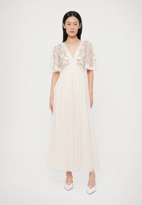 Μάξι φόρεμα σε ανοιχτό μπεζ, με διάφανα, κεντητά κοντά μανίκια, λαιμόκοψη σε σχήμα V και αέρινη πλισέ φούστα. Διακοσμημένο με λουλουδένια σχέδια.