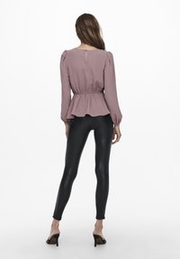 Eng anliegende mauvefarbene Bluse mit Puffärmeln und Schößchen an der Taille, kombiniert mit glänzenden schwarzen Leggings und Sandalen mit Absatz, Rückansicht.